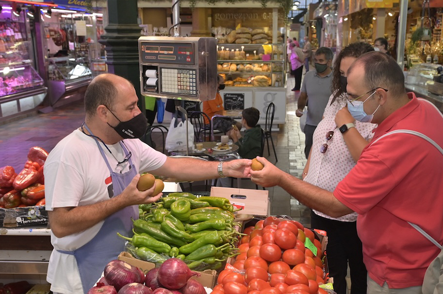 Kraampjehouder die fruit aan een klant serveert op een versmarkt.